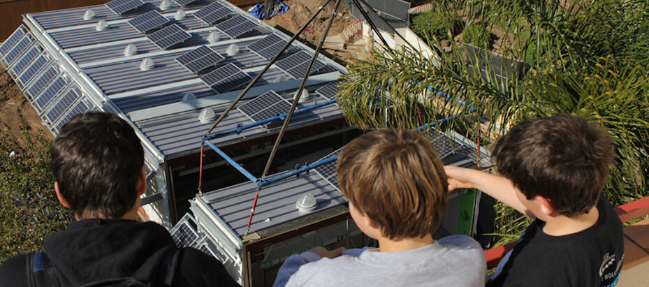 three school aged boys look down on solar panel-topped buildings